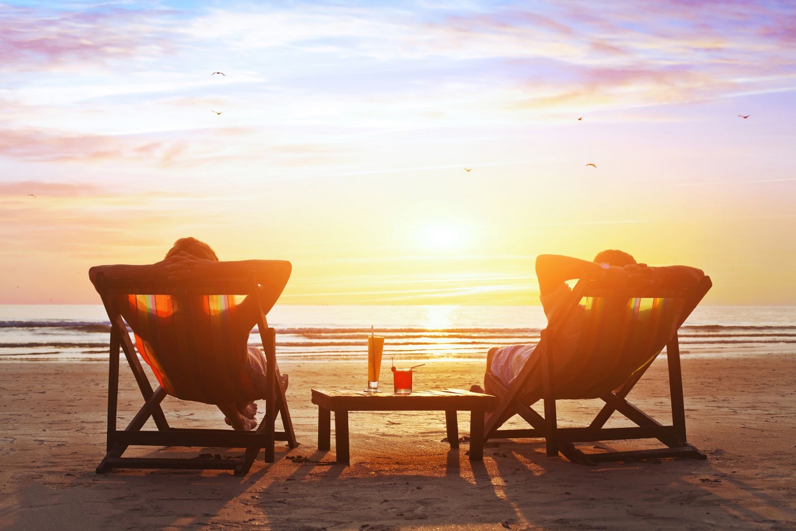 Twee mensen in strandstoel op het strand, ondergaande zon, zorgeloos dankzij Huisartsenzorg